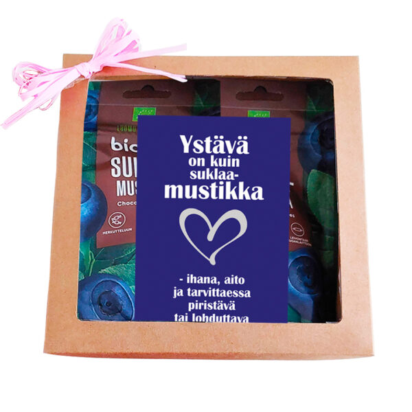 A charming cardboard gift box - chocolate bilberries with a clear window showcases two packs of chocolate-covered bilberries. The enclosed card, featuring a heart illustration, reads "Ystävä on kuin suklaamustikka - ihana, aito ja tarvittaessa piristävä tai lohduttava.